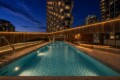 Nighttime rooftop pool with warm wooden walls and city skyscrapers in the background