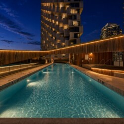 Nighttime rooftop pool with warm wooden walls and city skyscrapers in the background