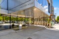 Front entrance of Vancouver House with glass doors, a metallic canopy, and reflective windows at 1480, showing trees and street reflections.