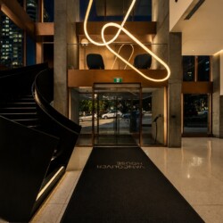 Modern hotel lobby with a curved black staircase, glass entrance, and a glowing loop sculpture overhead.