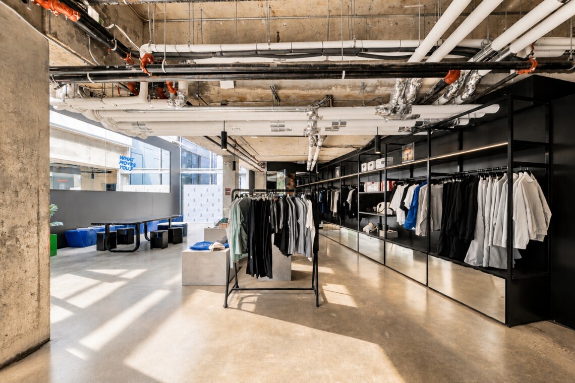 Industrial-style clothing store interior with black metal racks and a long wall of garments under an exposed-pipe ceiling.