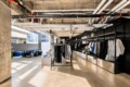 Industrial-style clothing store interior with black metal racks and a long wall of garments under an exposed-pipe ceiling.