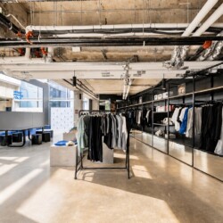 Industrial-style clothing store interior with black metal racks and a long wall of garments under an exposed-pipe ceiling.