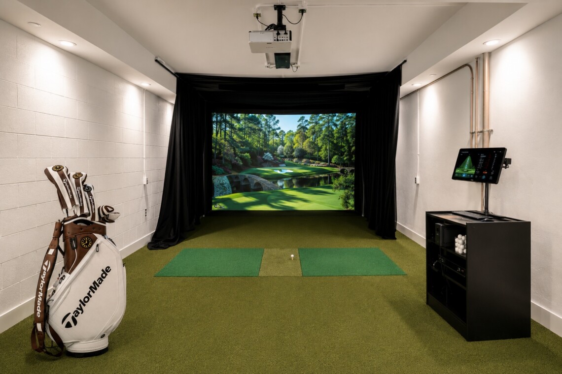 Indoor golf simulator room with a screensled virtual course, hitting mat, and projector above.