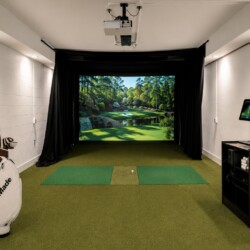 Indoor golf simulator room with a screensled virtual course, hitting mat, and projector above.