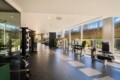 Bright gym interior with weight machines and cardio equipment along large windows overlooking an outdoor railing area.