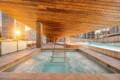 Rooftop pool under a warm wooden canopy, with a metal ladder and city high-rises in the background at sunset.