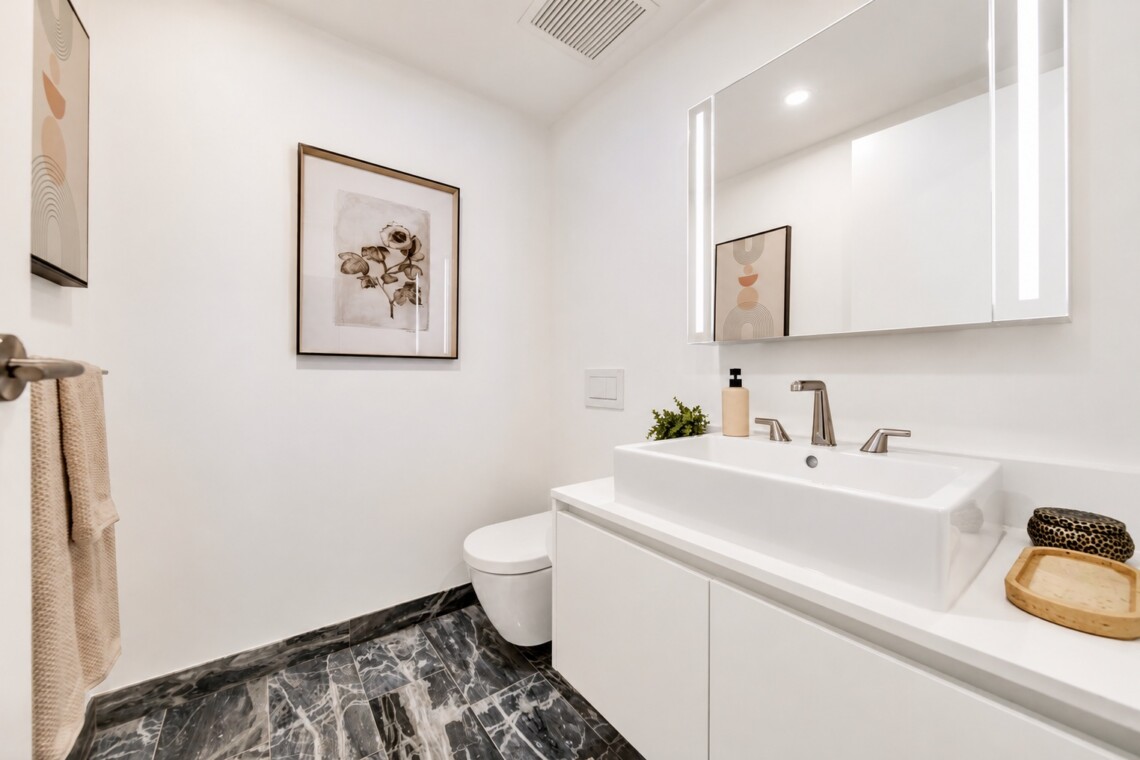 Minimalist white bathroom with a wide rectangular sink, two-handle faucet, backlit mirror, and marble-patterned floor.