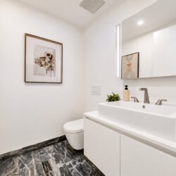 Minimalist white bathroom with a wide rectangular sink, two-handle faucet, backlit mirror, and marble-patterned floor.