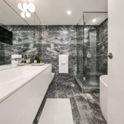Modern bathroom with marble walls and floor, white vanity, glass-enclosed shower, and a freestanding tub partially visible on the right.