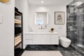 Modern bathroom with a white floating vanity, backlit mirror, and glass-walled shower on dark marble floors and walls, plus a wall-mounted toilet.
