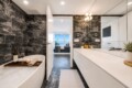 Modern bathroom with black marble walls, white vanity, and a bathtub; a wooden tray holds wine, a candle, and a rolled towel.