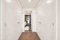 White-paneled hallway with doors on both sides, opening to a marble-tiled bathroom at the end; wooden floor in foreground.