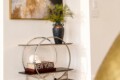 Decorative console table with a circular metal frame, vase of greenery, and a book titled 'New York' beneath a small skull ornament.