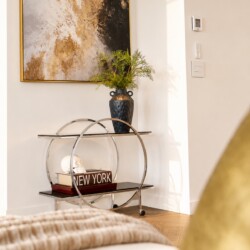 Decorative console table with a circular metal frame, vase of greenery, and a book titled 'New York' beneath a small skull ornament.