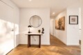 Entryway with a round mirror above a marble console table, black lamp, small plant, and a statue against white walls.
