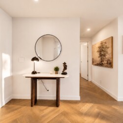 Entryway with a round mirror above a marble console table, black lamp, small plant, and a statue against white walls.