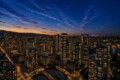 Downtown city skyline at dusk with illuminated high-rise buildings and a orange-hued horizon.