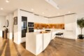 Modern white kitchen with a curved island, warm golden backsplash, and black bar stools.