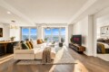 Bright open living room with beige sectional, colorful pillows, and a rug overlooking the city from large windows yes.