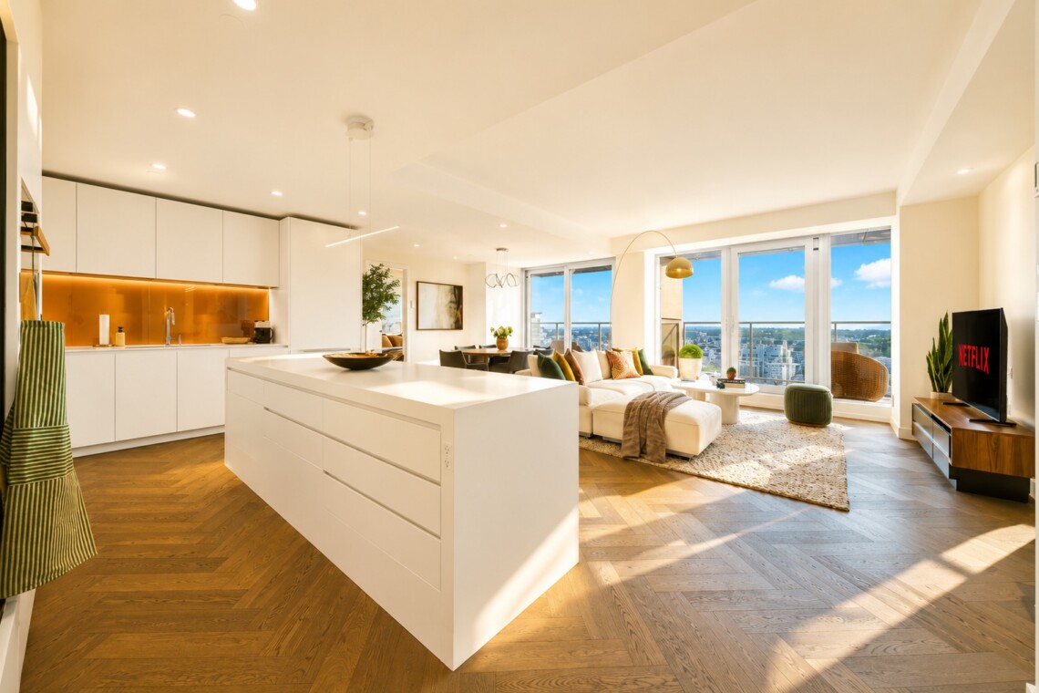 Bright open-plan kitchen and living area with a large white island, white cabinets, and a cozy seating area by expansive windows overlooking the city skyline