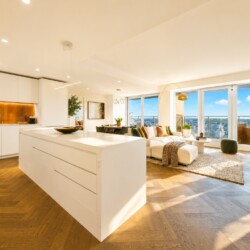 Bright open-plan kitchen and living area with a large white island, white cabinets, and a cozy seating area by expansive windows overlooking the city skyline