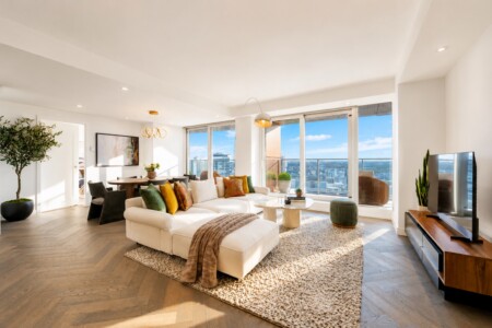 Bright modern living room with a white sectional, colorful cushions, and large windows overlooking the city skyline.