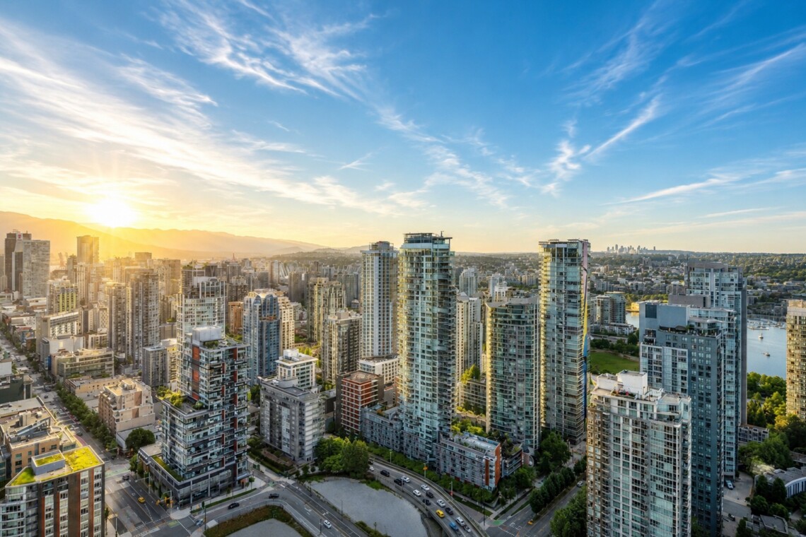Sunlit city skyline with tall residential towers and a river in the distance at sunset.