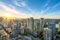 Sunlit city skyline with tall residential towers and a river in the distance at sunset.
