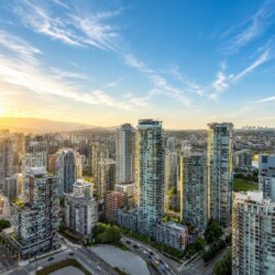 Sunlit city skyline with tall residential towers and a river in the distance at sunset.