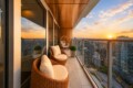 Sunset view from a high-rise balcony with wicker chairs and beige cushions overlooking a city skyline.
