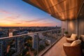 Balcony view at sunset: modern terrace with wicker chairs overlooking a city and river below.