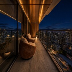 Night view from a high-rise balcony with two wicker lounge chairs and warm lighting over a cityscape at night.