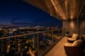Nighttime city skyline viewed from a high balcony with wicker chairs and a glass railing.
