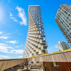 Modern high-rise buildings under a bright blue sky with a low wooden walkway in the foreground.