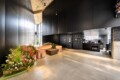 Modern black-walled lobby with pink curved benches and a central coffee table, next to a lush flower bed.