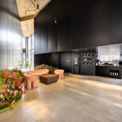 Modern black-walled lobby with pink curved benches and a central coffee table, next to a lush flower bed.