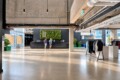 Modern reception area with a black counter and a green vertical garden behind it; two visitors stand at the desk in a concrete-ceiling lobby.