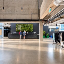 Modern reception area with a black counter and a green vertical garden behind it; two visitors stand at the desk in a concrete-ceiling lobby.