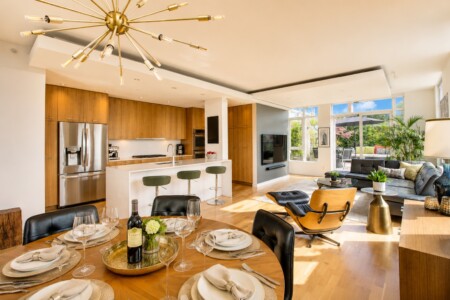 Open-concept kitchen and living area with wooden cabinets, stainless steel fridge, white island, and a round dining table set for six.