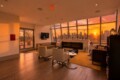 Cozy modern lounge with a marble fireplace, beige chairs, and a city skyline at sunset through large angled windows