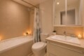 Modern beige-tiled bathroom with a bathtub on the left, a shower curtain, and candles along the edge for ambient lighting.