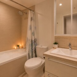 Modern beige-tiled bathroom with a bathtub on the left, a shower curtain, and candles along the edge for ambient lighting.
