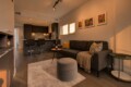 Open-concept living area with a dark kitchen island, two bar stools, gray sofa, and three colorful framed artworks.
