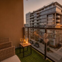Cozy balcony seating with candles and wine on a small table, overlooking modern apartment buildings at sunset.