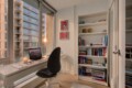 Bright home office with a white desk by a large window, a laptop, glasses, and a lit candle, overlooking a cityscape at sunset.