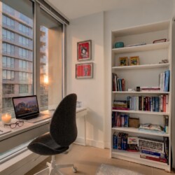 Bright home office with a white desk by a large window, a laptop, glasses, and a lit candle, overlooking a cityscape at sunset.