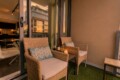 Cozy balcony seating with wicker chairs, cushions, wine bottles, and a lit candle on a small table as evening light shines on neighboring buildings