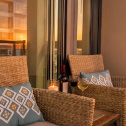 Cozy balcony seating with wicker chairs, blue patterned cushions, a candle, wine bottle and two glasses at sunset.