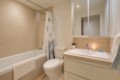 Modern bathroom with a tub, rainfall showerhead, and patterned shower curtain beside a white toilet and beige tiled walls.